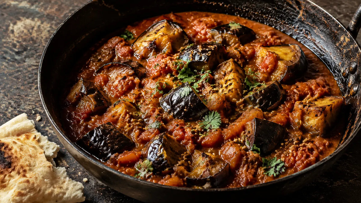 Bengali Five Spice aubergine and tomato curry with toasted whole seeds and coriander in a rustic iron pan.