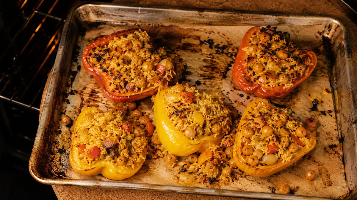 Red and yellow peppers stuffed with biryani rice, chickpeas and vegetables on a rustic oven tray.