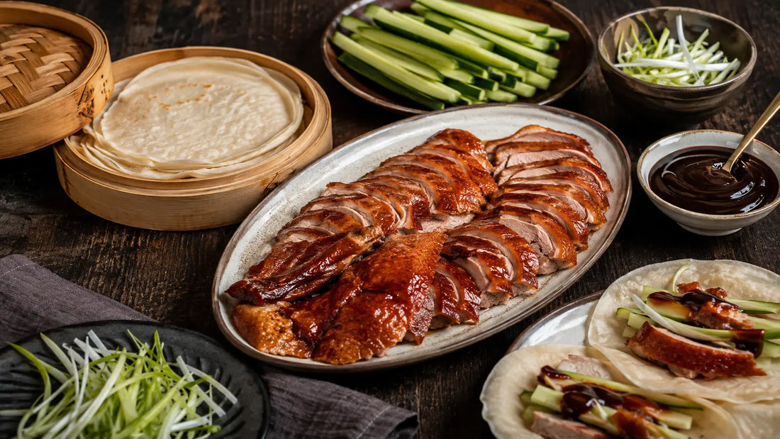 Chinese Five Spice roast duck pancakes with cucumber, spring onions and hoisin sauce on a rustic sharing table.