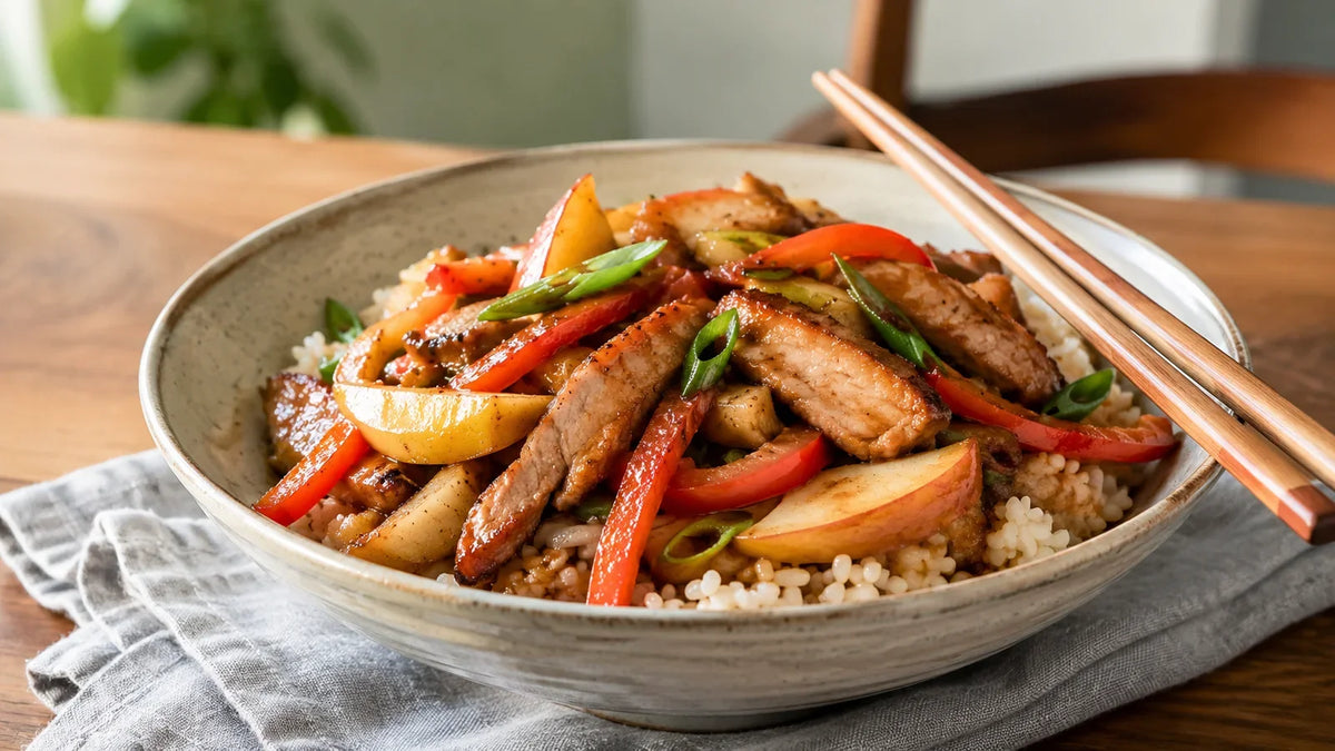 Mixed sweet spice pork and apple stir-fry with red pepper and spring onion, served over rice in a ceramic bowl.