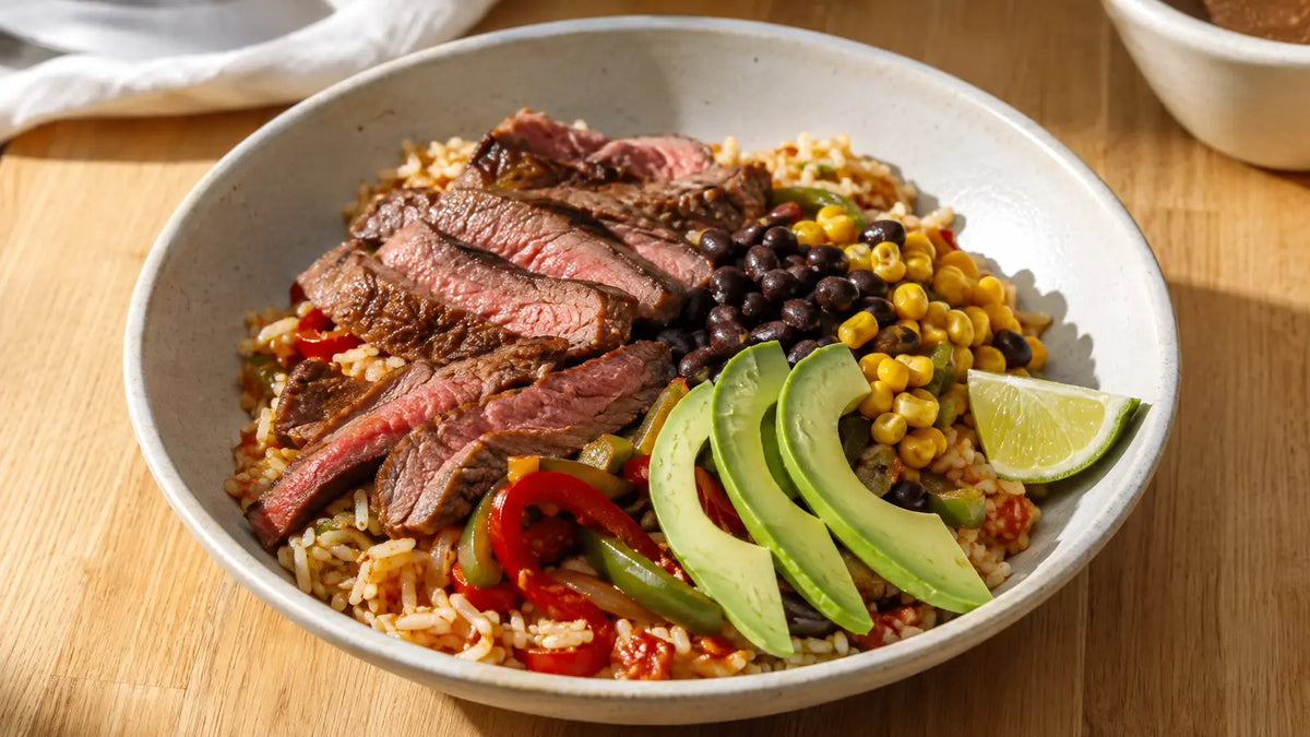 Steak and pepper fajita rice bowl with sliced beef, seasoned rice, black beans, sweetcorn, avocado and lime.