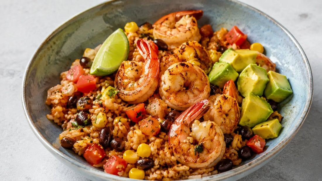 Taco-spiced prawn and avocado rice bowl with black beans, sweetcorn, tomato and lime in a handmade ceramic bowl.