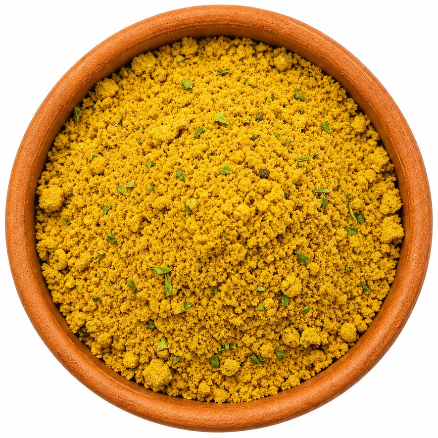 Top-down view of Bangalore spice blend in a terracotta bowl, showing a vibrant golden seasoning with fine texture and scattered herb flakes on a clean white background.